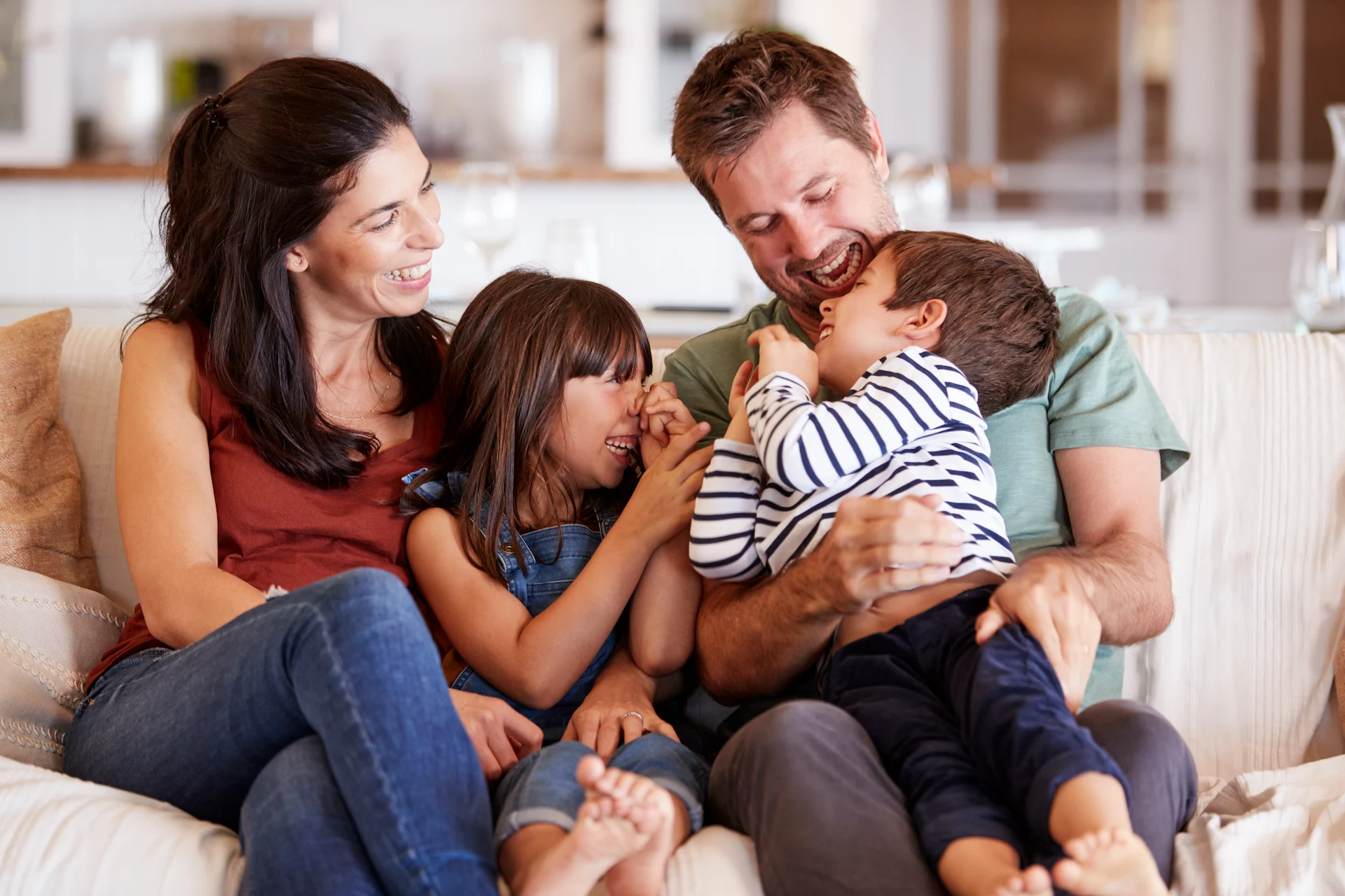 Two smiling parents playing with their young son and daughter on the couch at home